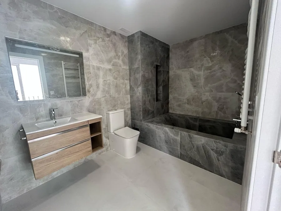 Baño completo reformado con mueble de lavabo en madera y bañera de obra en piedra natural, JJ Reformas Valencia